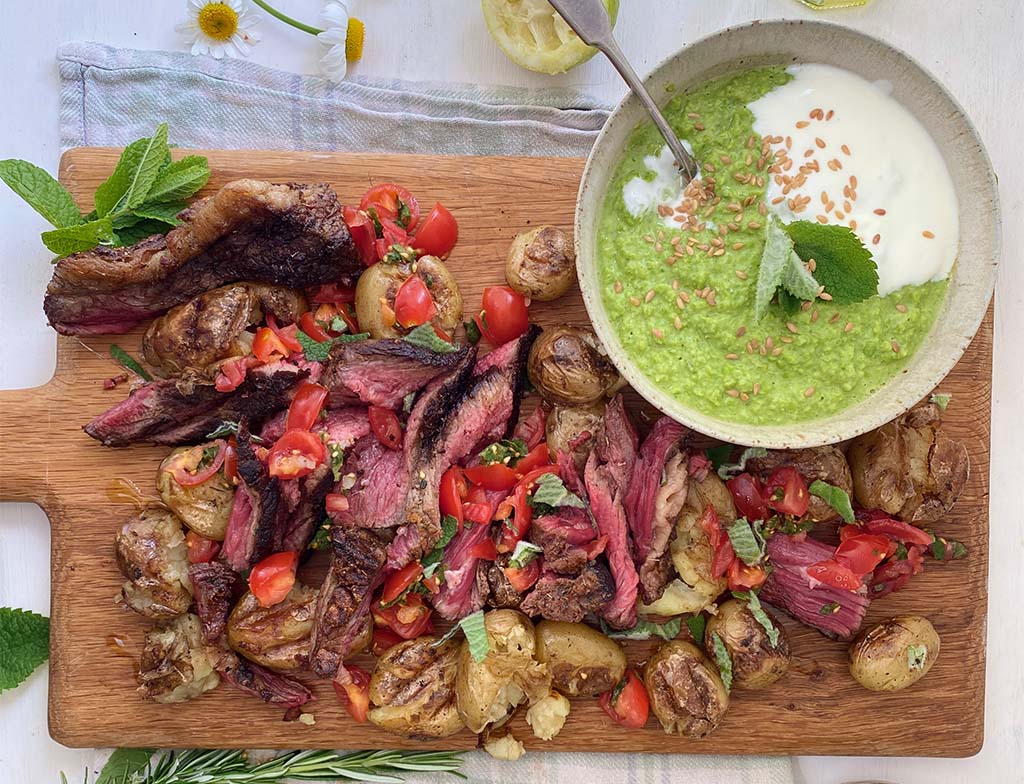 An image of barbecued steak with smashed rosemary potatoes and pea guacamole on a wooden board.