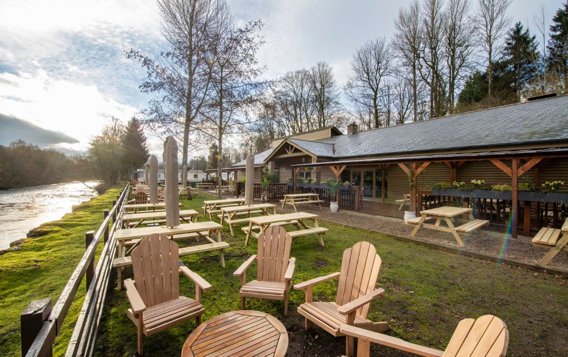 Holiday park beer garden by a river with tables and chairs outside on the grass
