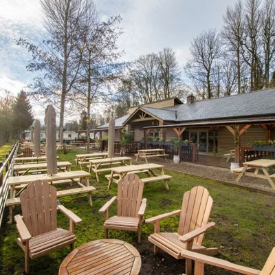 Holiday park beer garden by a river with tables and chairs outside on the grass