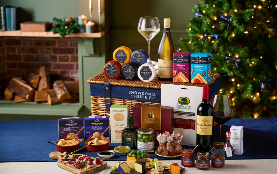 A hamper of cheese, chutneys, biscuits and wine with a Christmas tree in the background