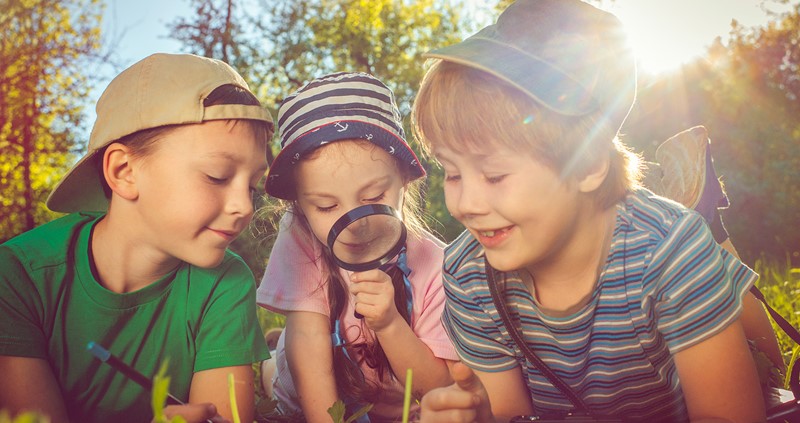 A photo of three children looking at something through a magnifying glass.