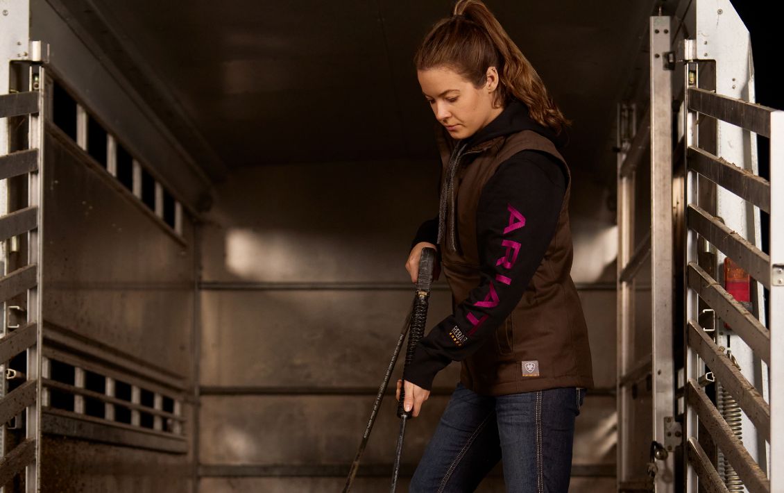 Woman wearing an Ariat top and cleaning out a horse box