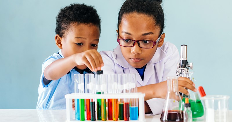 Two children conducting a science experiment. In front of them are many test tubes with coloured liquid inside them.