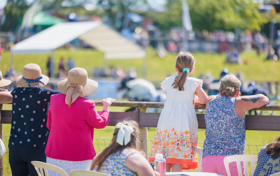 People standing and looking into an outdoor arena at a country show on a sunny day