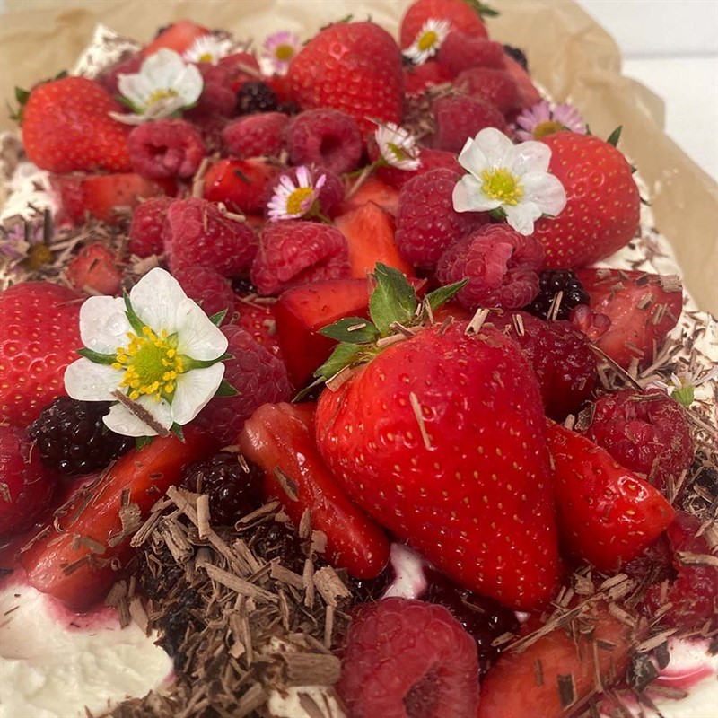 An image of the summer berry chocolate swirl meringue traybake, with strawberries, raspberries and flowers